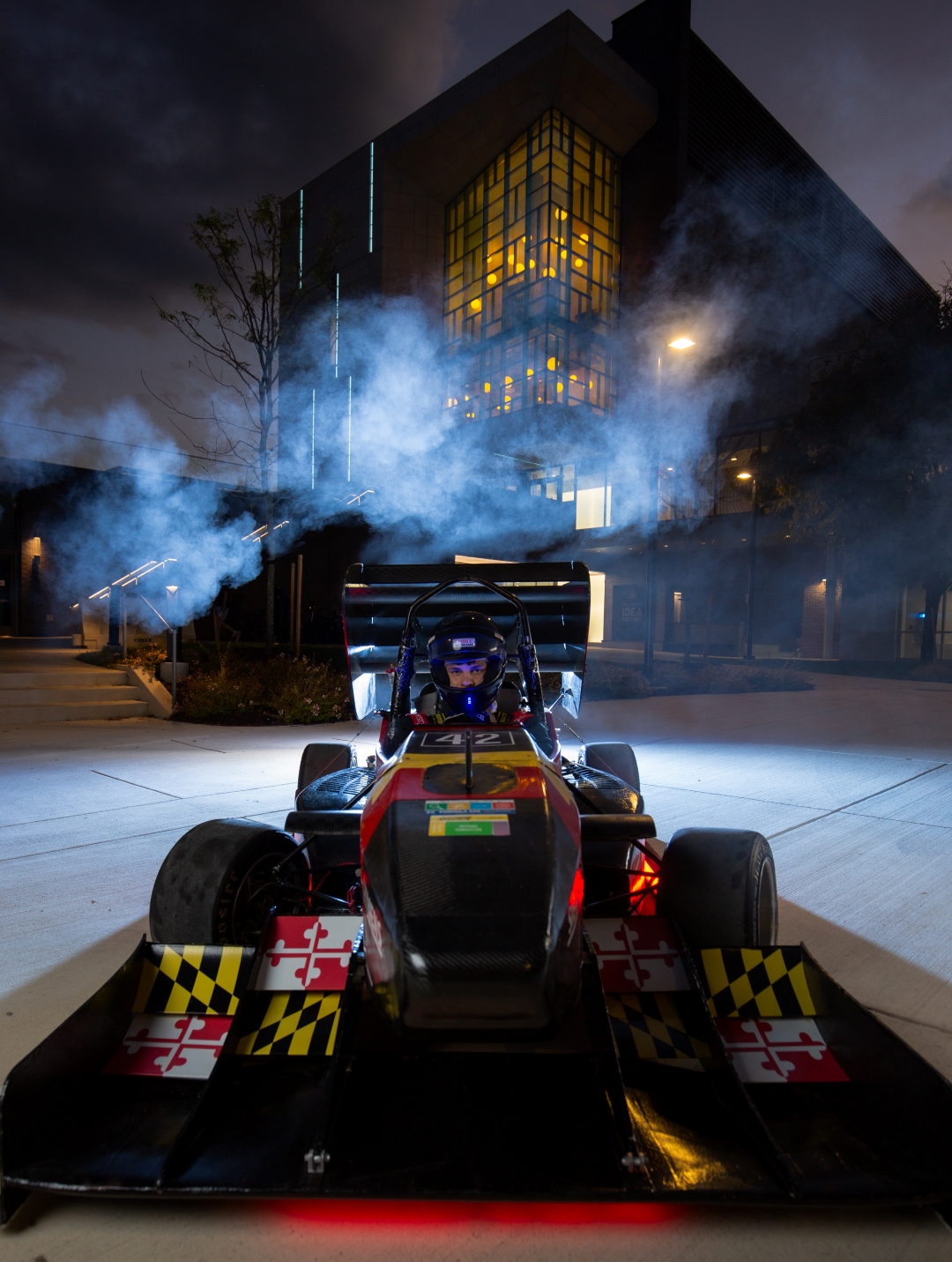 a Terps Racings electric vehicle revs vapor into the night sky in front of the IDEA factory