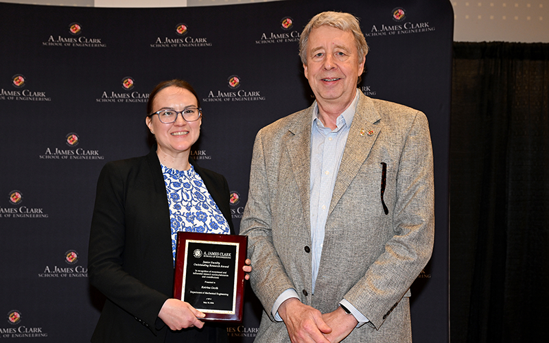 Katrina Groth stands next to Rob Briber in front of a Maryland Engineering backdrop with her award plaque in her hands