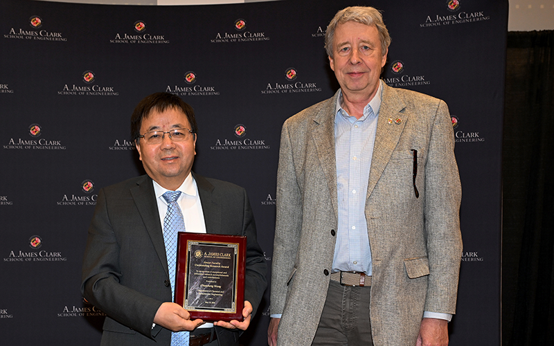 Chunsheng Wang stands with Rob Briber in front of a Maryland Engineering backdrop holding their award plaque