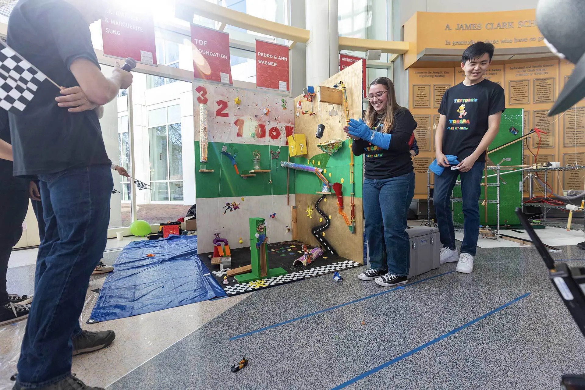 Isabelle LaManna ’26 (center), captain of the team from the Department of Materials Science and Engineering, applauds as its toy car rolls across the floor in the Kim Building atrium.