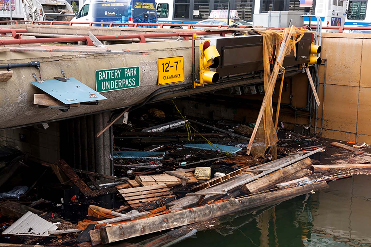 Photo of a flooded underpass with planks of wood and other debris floating on the water. White text on a green street sign reads "Battery Park Underpass"