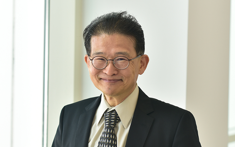 Dr. Hwang smiles in glasses with a black suit and black and white tie on