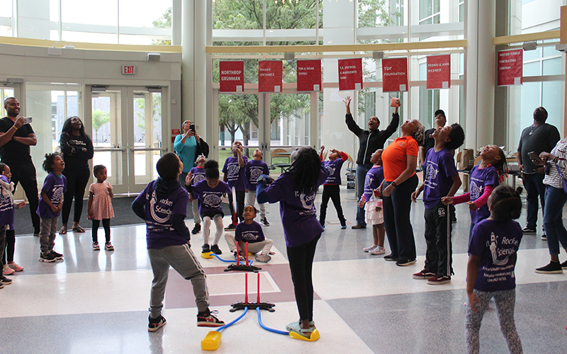 Students and teachers look up, cheering a model rocket launch