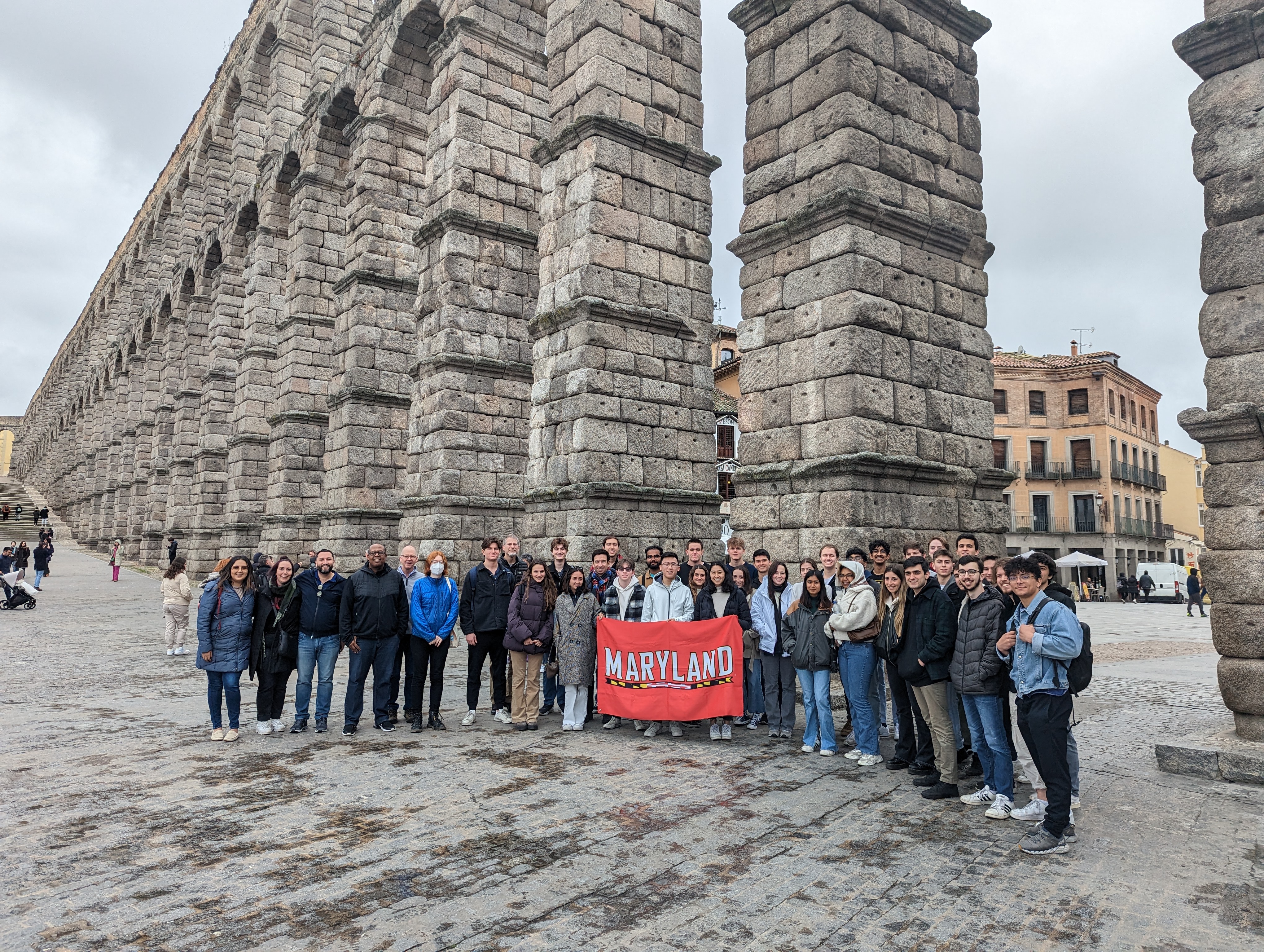 Maryland student, faculty and staff holding a Maryland flag in Segovia in front of the aquaduct.