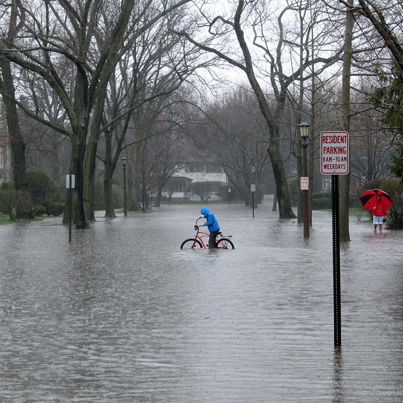 A person wearing a blue jacket rides a red bicycle through a flooded street