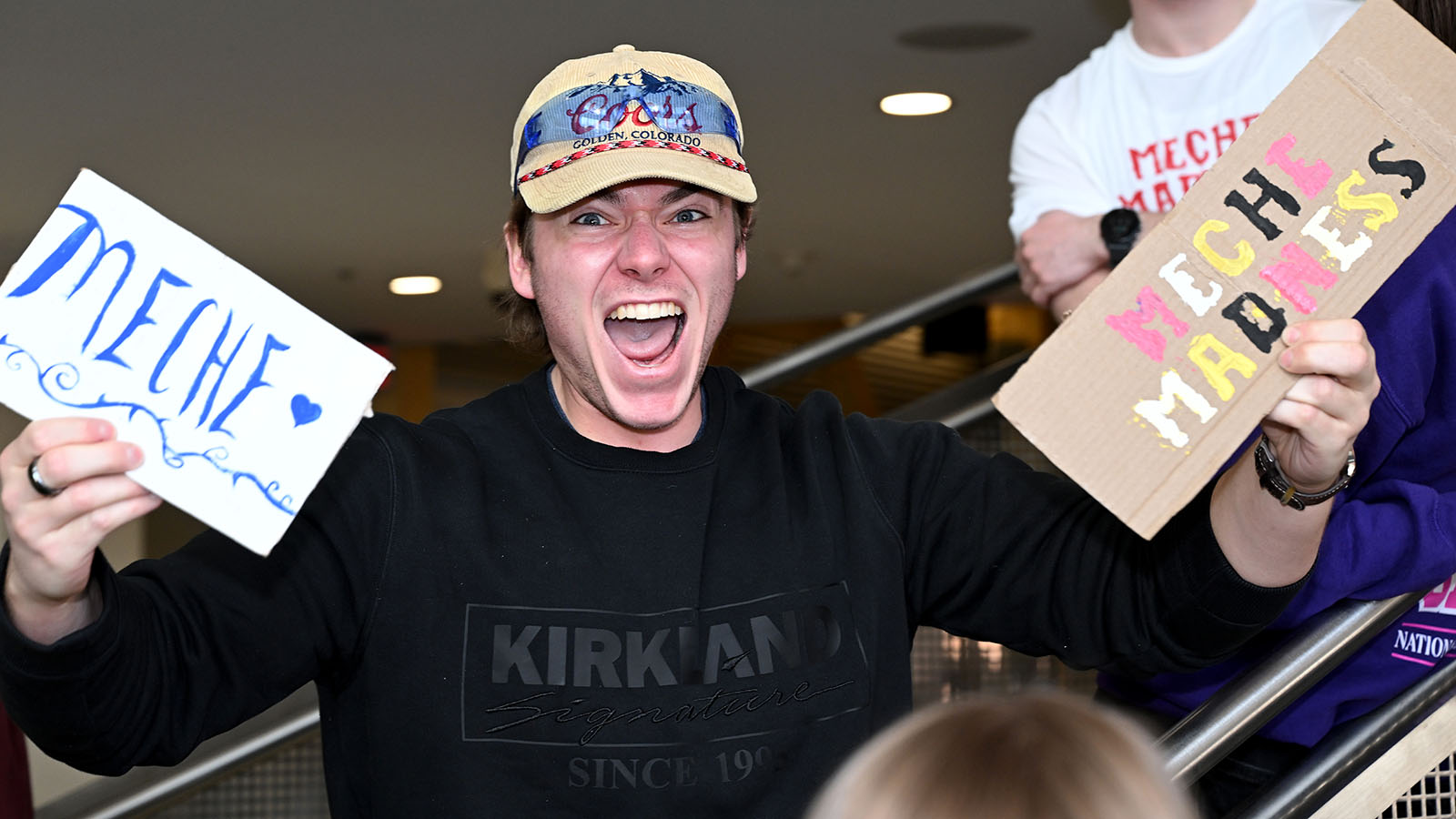 A student holding two signs yells in support of his favorite team