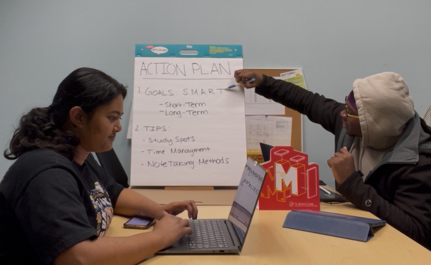 Two APCs working together, one on a laptop and one pointing to a board that says "Action Plan".