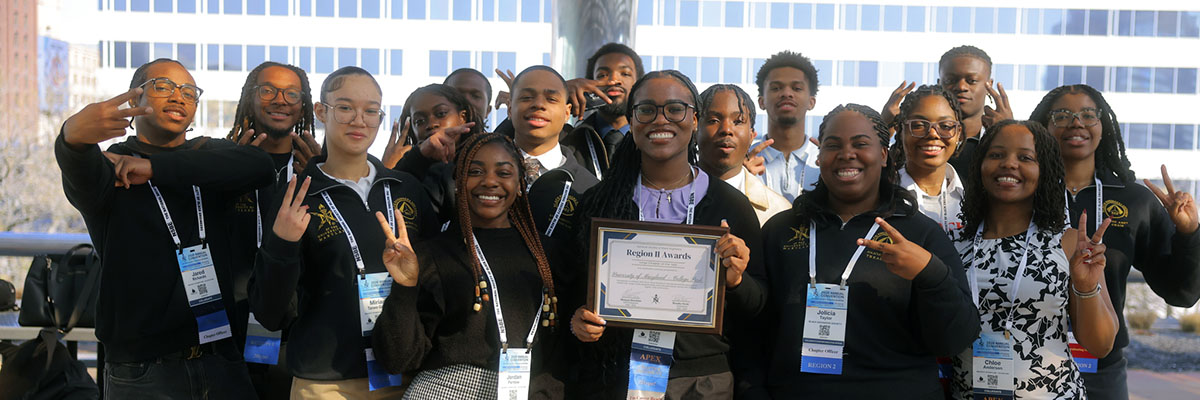 Sixteen students make peace signs with their fingers. One holds a framed award with the text Region II Awards
