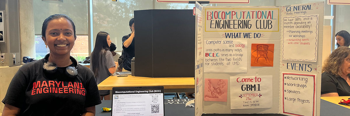 A student in a Maryland Engineering shirt stands by a trifold poster that reads Biocomputational Engineering