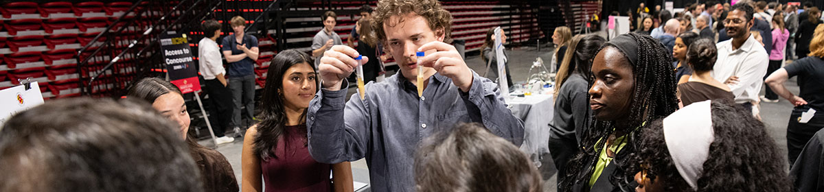 A bioengineering student holds up two vials as attendees watch