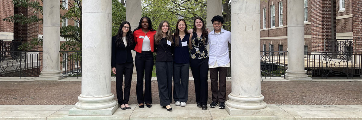 Six students pose between columns on the UMD campus