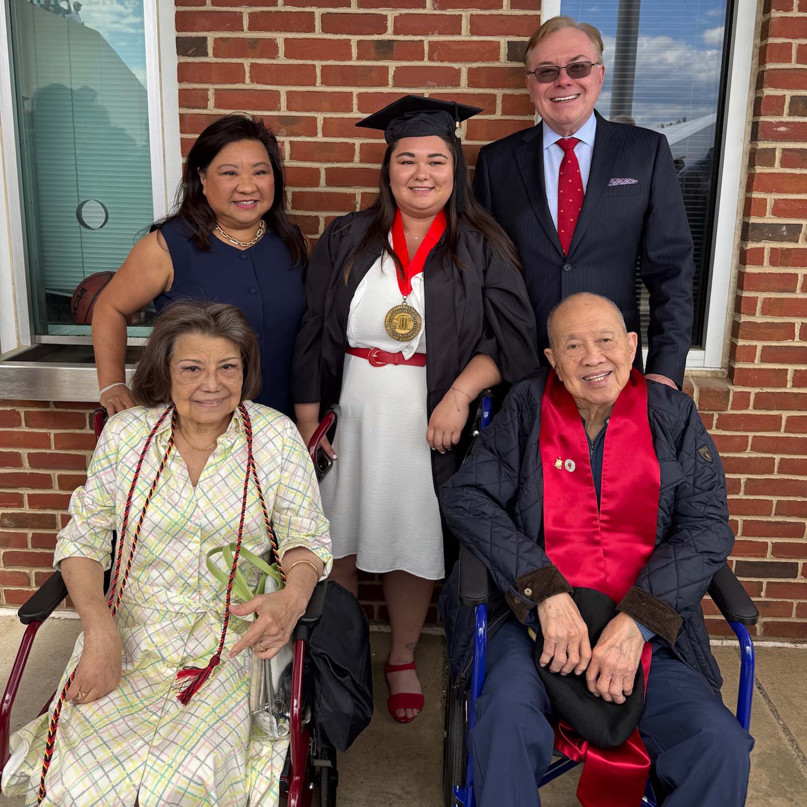 Chelsea Neumann wearing graduation regalia, posing with family members