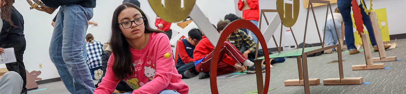 A student sits on the floor playing with an engineering kit
