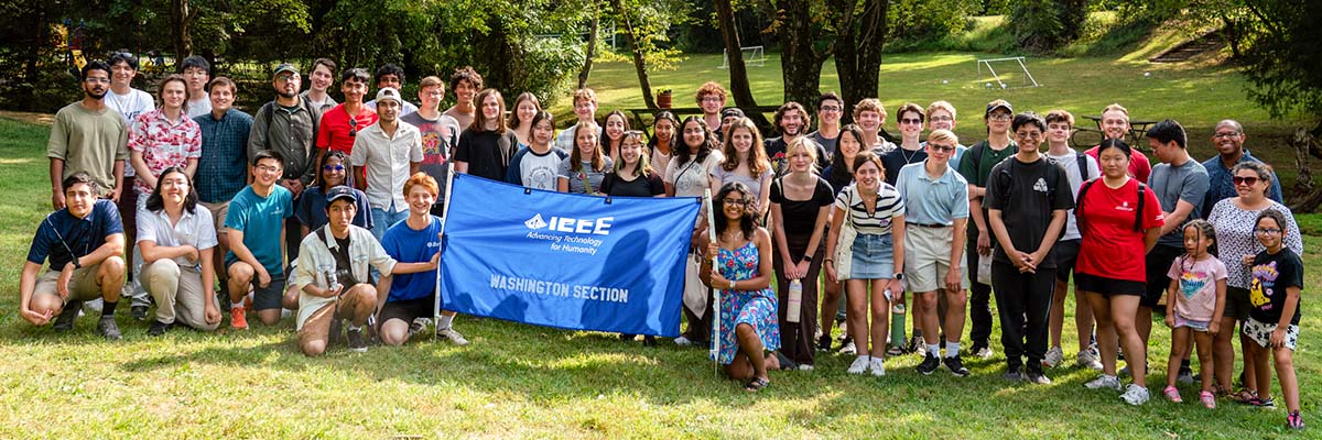 Dozen of students pose on the grass alongside a banner reading IEEE Washington Section