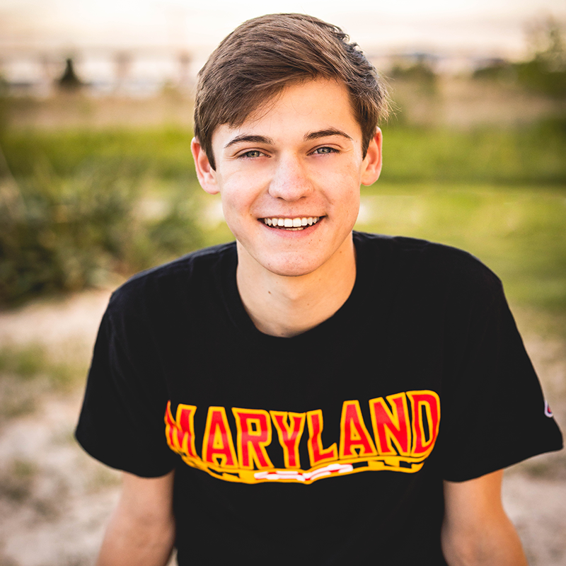 student poses with arms bracing themselves in a black University of Maryland tshirt