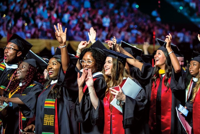 group of students smiling and waving wearing graduation regalia, with some also wearing kente cloths
