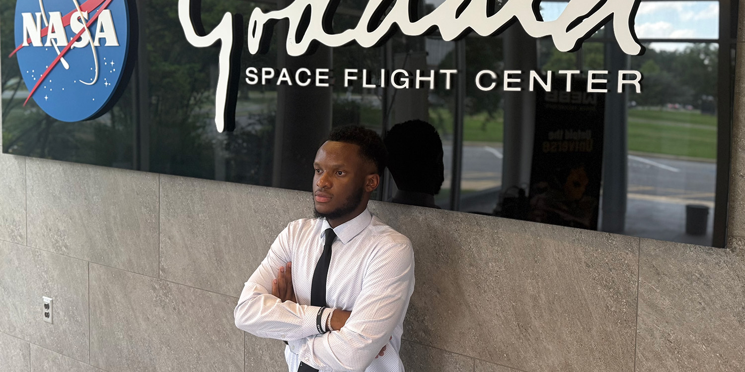 Joshua Budram stands under a sign for the NASA Goddard Space Flight Center