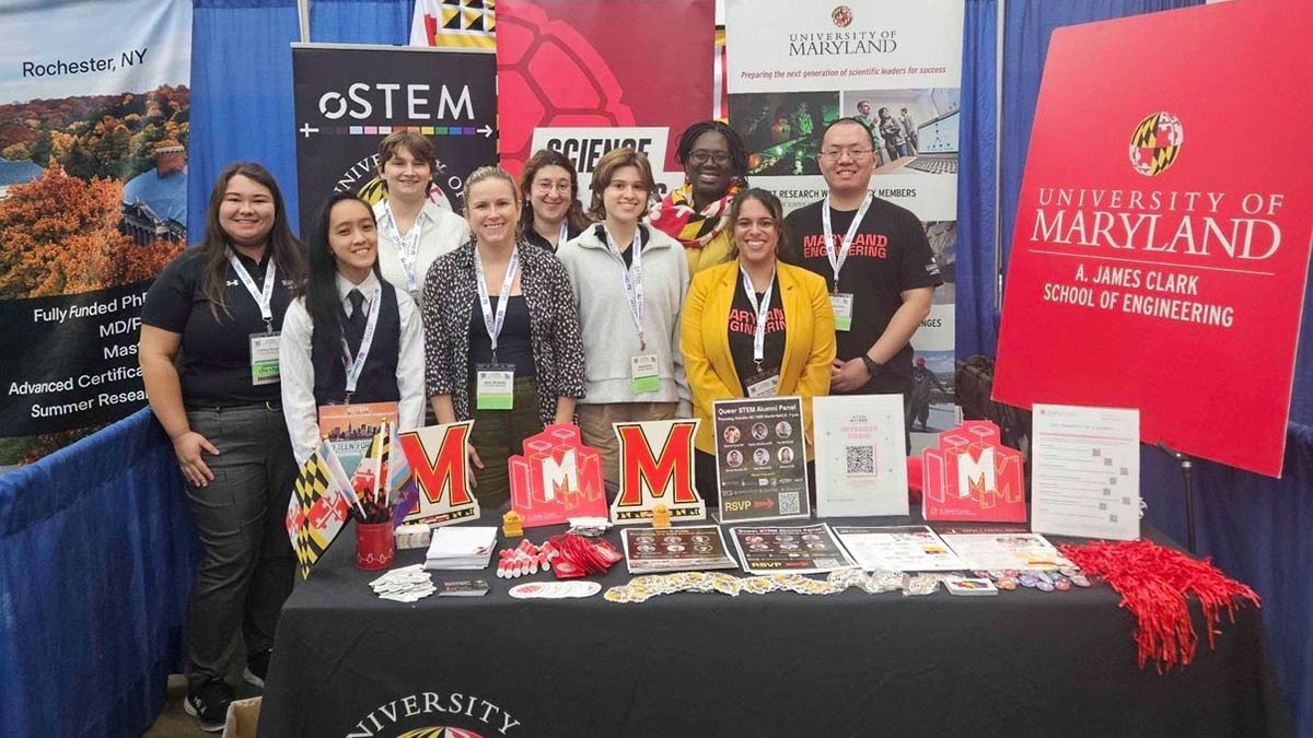 Eight staff and students pose behind an oSTEM Maryland Engineering table