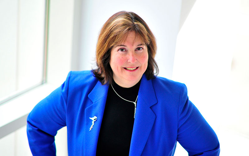 headshot of Maureen Meyer in a blue blazer with her hands propped on her hips