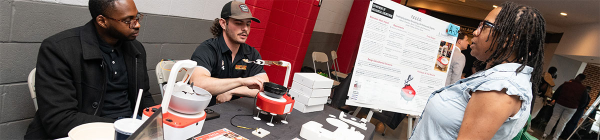 Two mechanical engineering students show their feeding device to an attendee