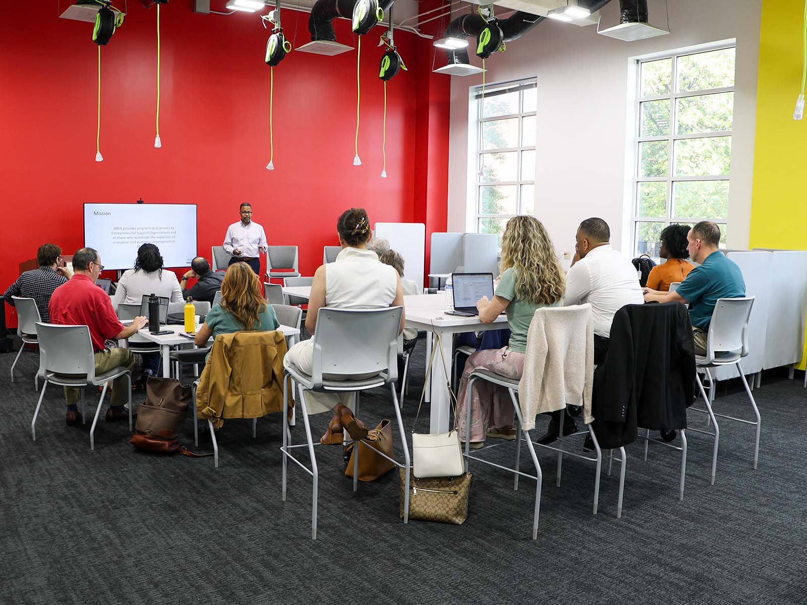 People in a well-lit room listen to a lecture
