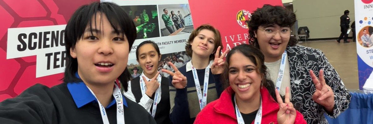 Four students and a staff member make funny faces and give the peace sign with their hands