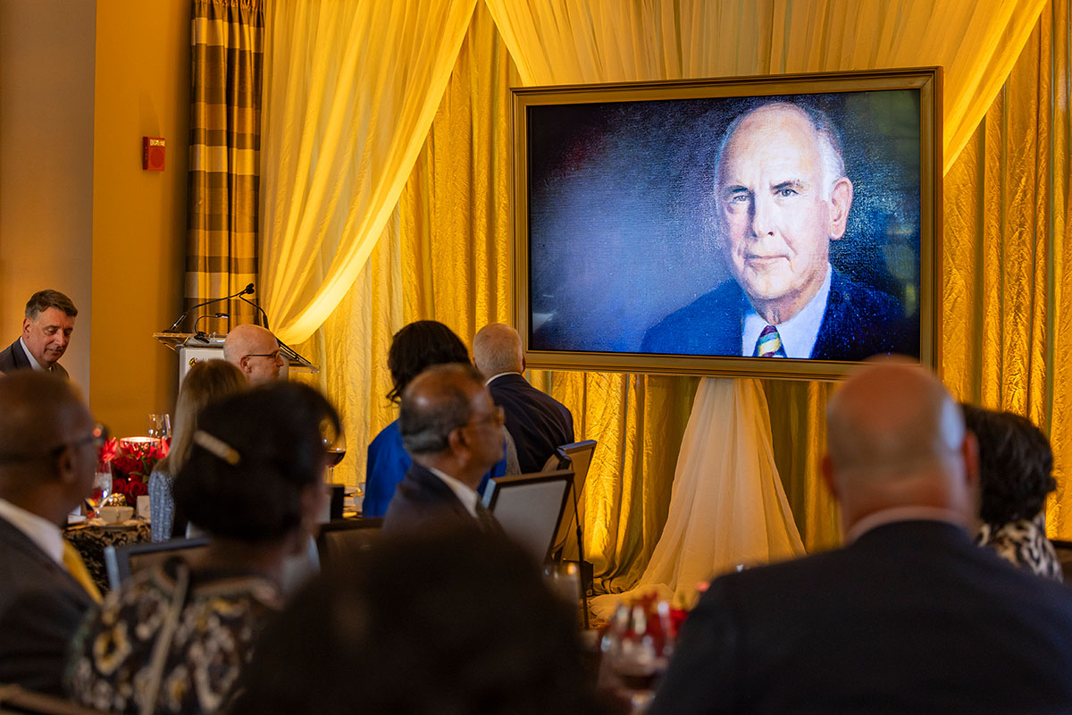 A painted portrait of A. James Clark with seated guests admiring it