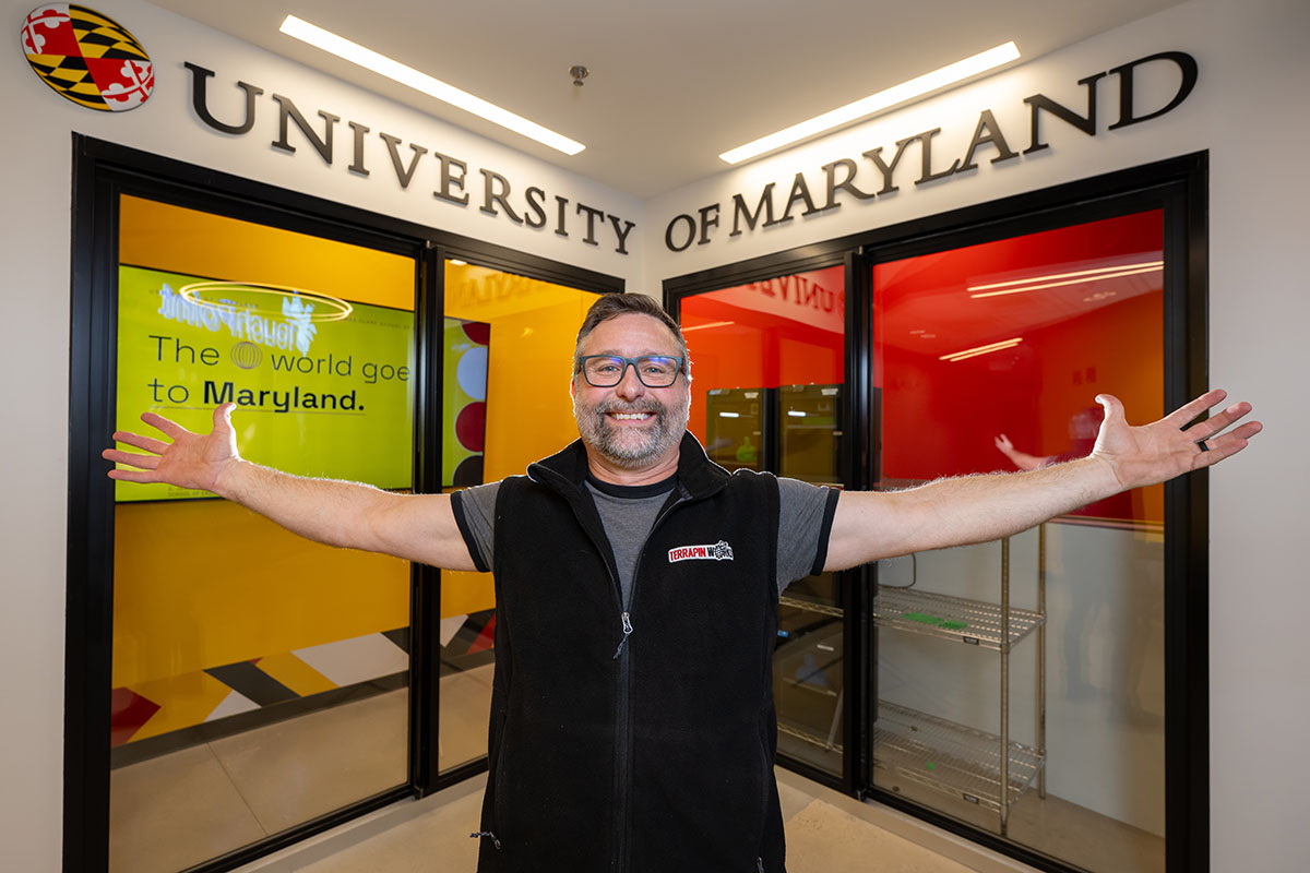 Man with outstretched arms under sign reading University of Maryland