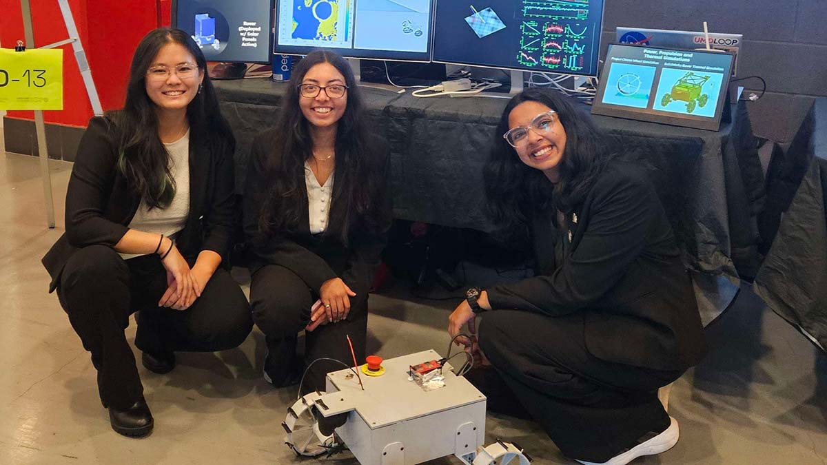 Three students kneel by a small robot