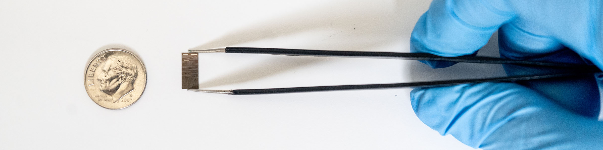 A small computer chip held by tweezers, held by a dime for size comparison