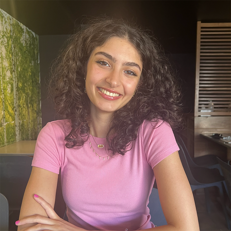 student in picture shirt poses alone for photo with arms crossed