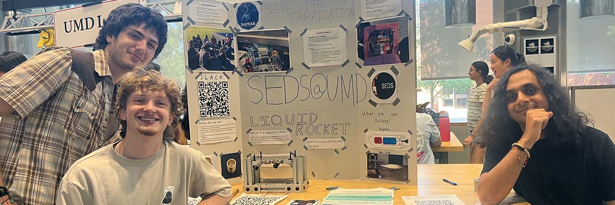 Three students pose by a trifold poster that reads SEDS@UMD: Liquid Rocket