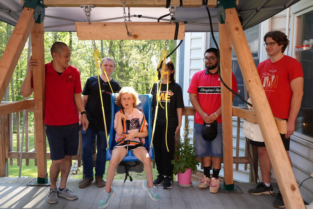 Nguyen and students stand by Avaleigh who is in the swing
