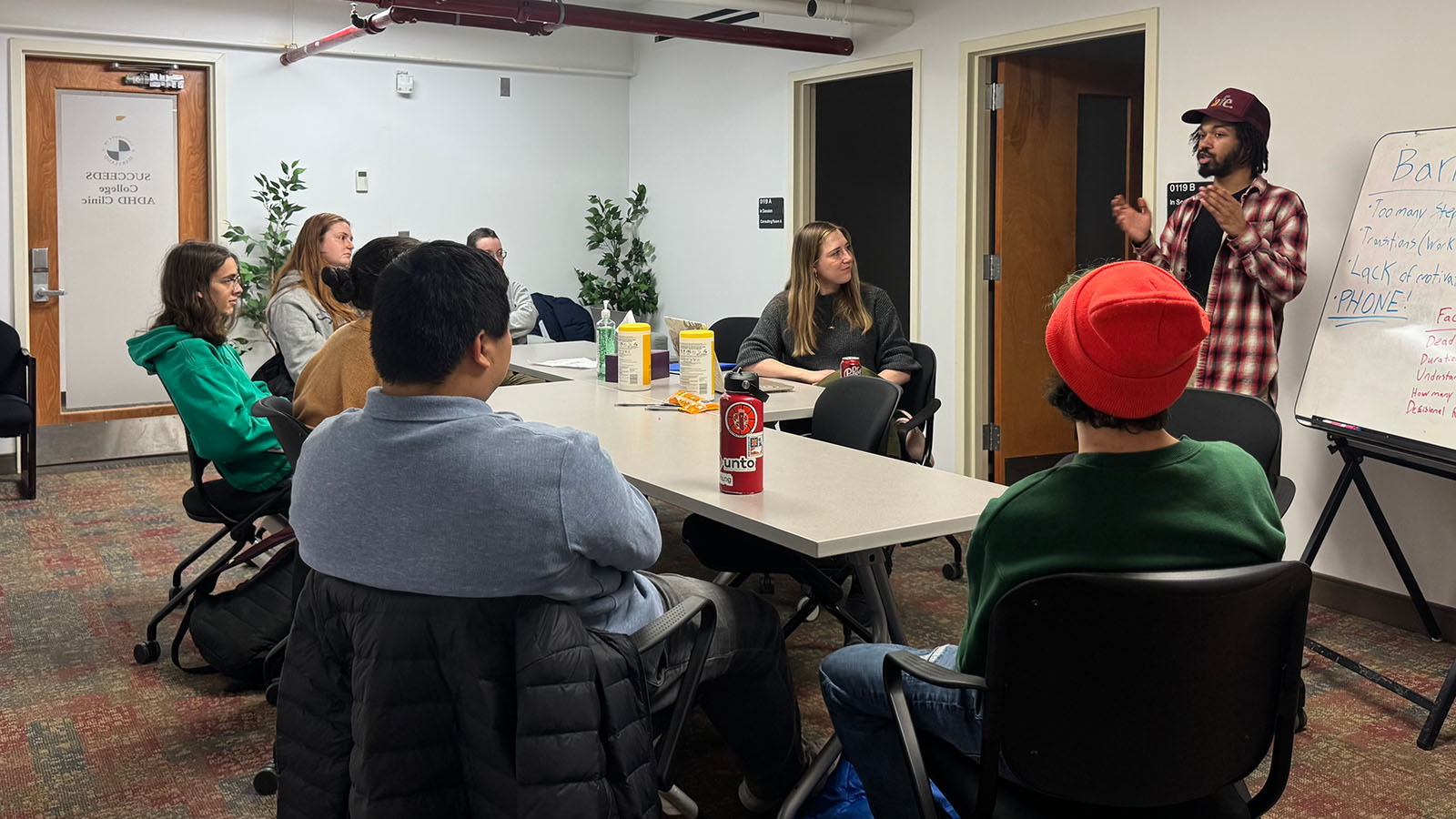 Students sit a table as an instructor stands and talks