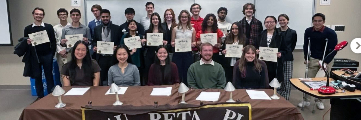 Nine students hold certificates, posing in a row between two rows of other students