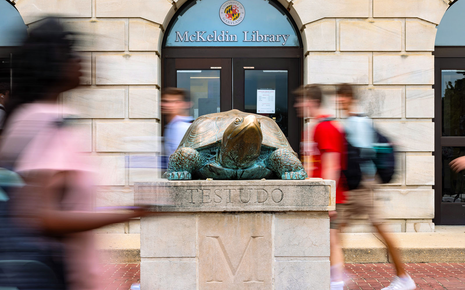 Statue of Testudo in front of McKeldin Library with blurs of students walking by