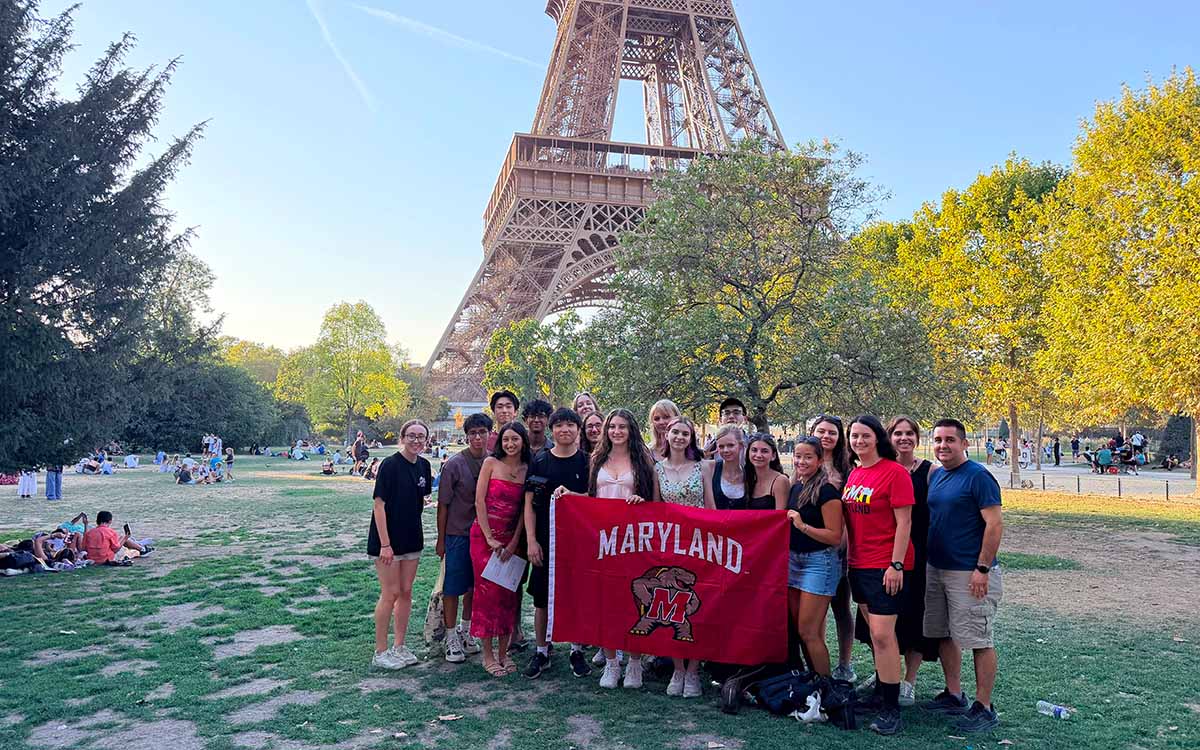 A group of students hold a University of Maryland banner in front of the Eiffel Tower