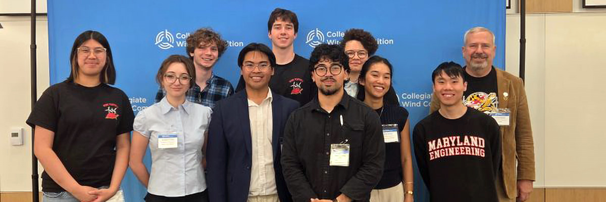 Nine students and an advisor stand before a blue Collegiate Wind Competition back drop
