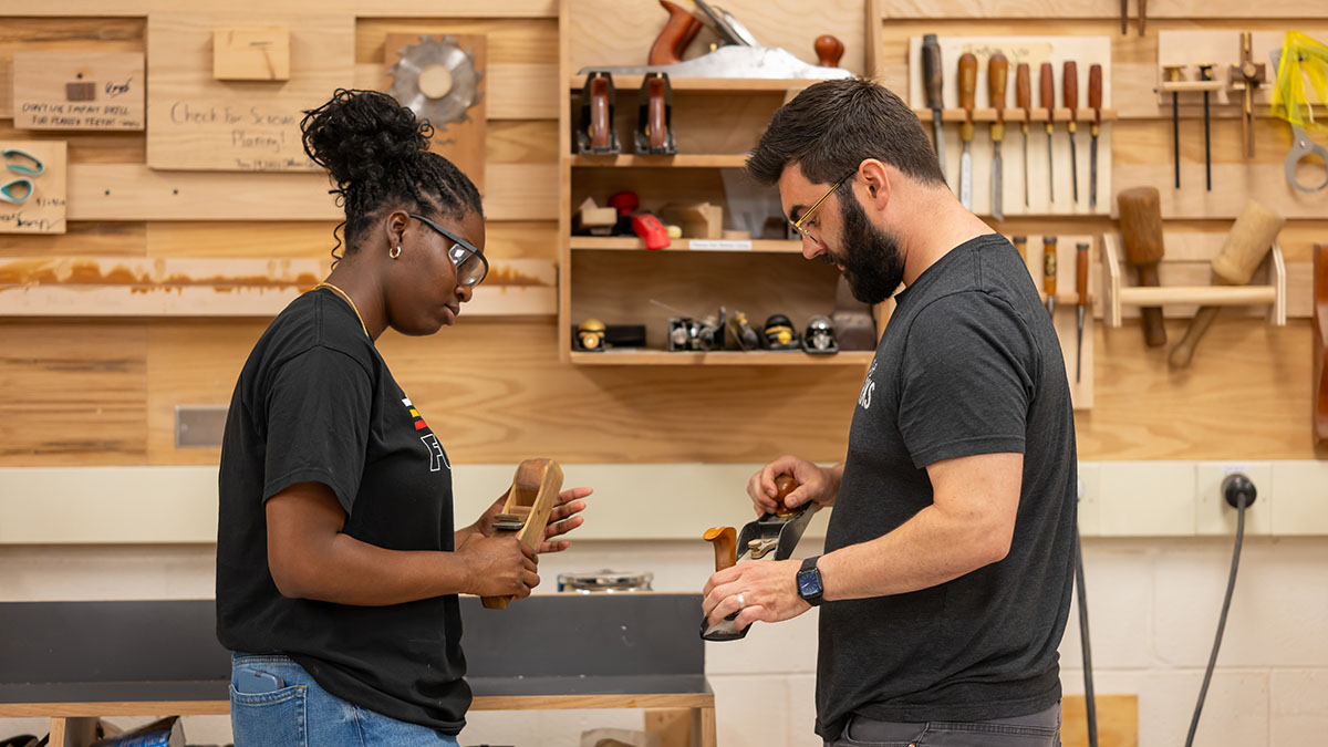 Two people with safety glasses look at woodworking tools